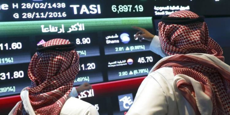 Visitors stand and watch stock movements displayed on large video screens inside the Saudi Stock Exchange, also known as the Tadawul All Share Index in Riyadh, Saudi Arabia, on Monday, Nov.28, 2016. The Tadawul All Share Index advanced 26 percent since Saudi Arabias record-breaking bond sale last month, the most in the world during that period. Photographer Simon Dawson/Bloomberg