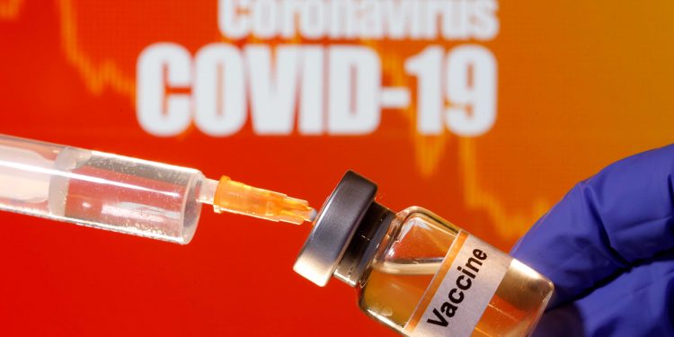 FILE PHOTO: A small bottle labeled with a "Vaccine" sticker is held near a medical syringe in front of displayed "Coronavirus COVID-19" words in this illustration taken April 10, 2020. REUTERS/Dado Ruvic/Illustration -/File Photo