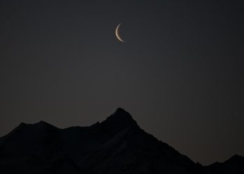 A picture taken early on February 27, 2022 shows a crescent of moon above the 4506 meters high Weisshorn mountain in the Swiss alps from Crans-Montana, Switzerland. (Photo by Fabrice COFFRINI / AFP)