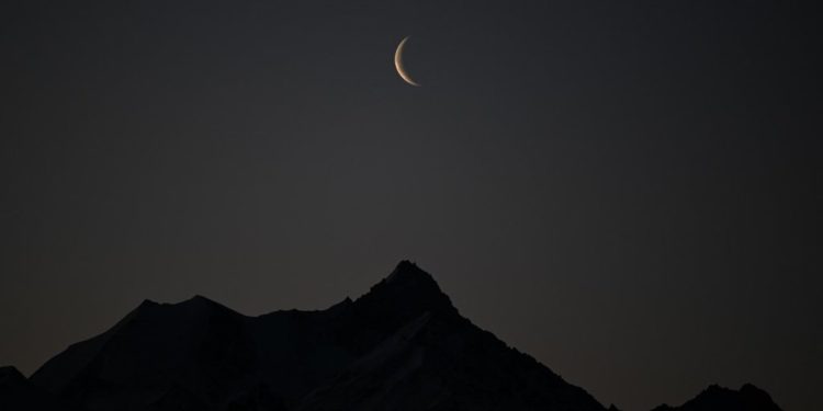 A picture taken early on February 27, 2022 shows a crescent of moon above the 4506 meters high Weisshorn mountain in the Swiss alps from Crans-Montana, Switzerland. (Photo by Fabrice COFFRINI / AFP)
